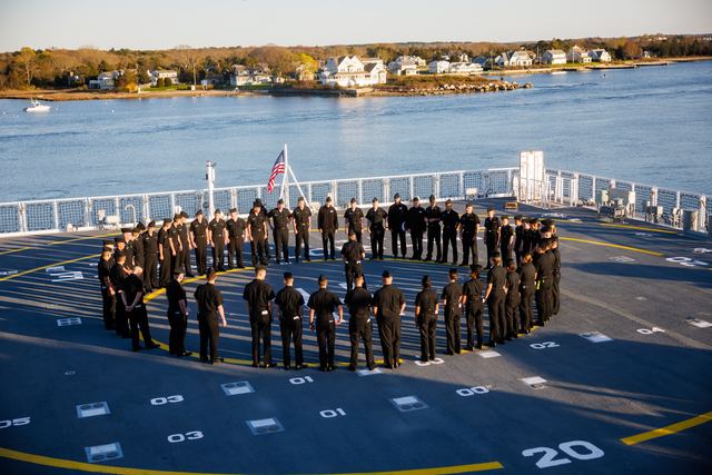 Cadets standing in formation on the ship's deck with the harbor behind them