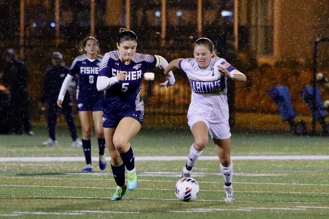 A Buccaneer racing a St. John Fisher defender to the ball in the rain